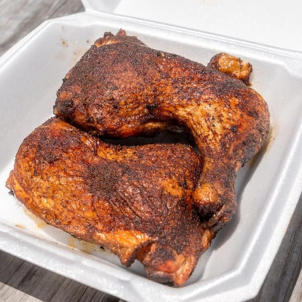 Two perfectly smoked chicken leg quarters with crispy, seasoned skin in a white takeout container.