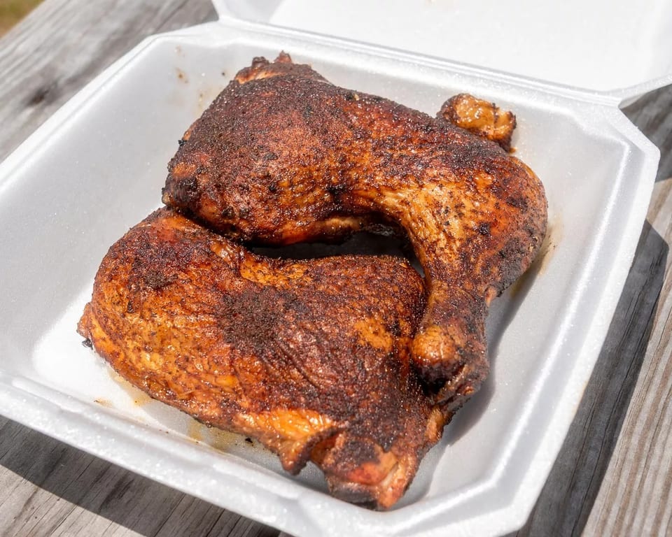 Two perfectly smoked chicken leg quarters with crispy, seasoned skin in a white takeout container.