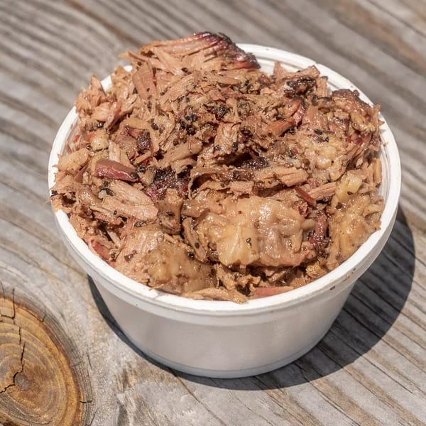 A white bowl filled with shredded, seasoned barbecue meat sits on a rustic wooden surface.