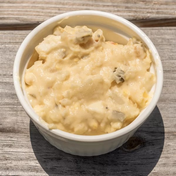 Creamy potato salad with visible chunks of potato and relish in a white bowl on a wooden surface.