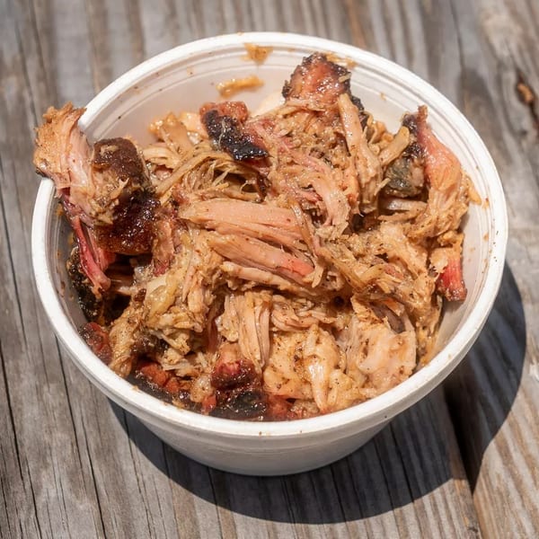 A white bowl filled with juicy pulled pork, showing crispy edges and tender meat, on a wooden table.